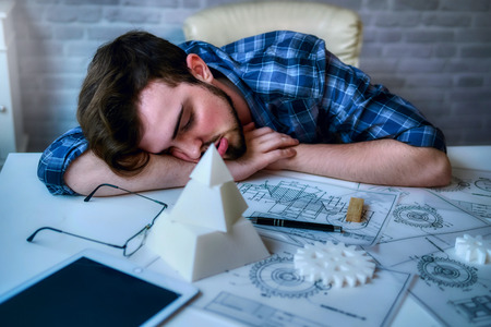 Engineering man working overwork and sleep on the desk with blueprint mechanical parts in office. having a bad stress and overwork concept - Imageの写真素材