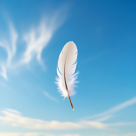 A single white feather, its barbs soft and slightly frayed, is captured in mid-air against a vivid blue sky. The sky is adorned with thin, streaky clouds that add a dynamic element to the serene backdrop. The feather appears to be gently carried by the wind, embodying a sense of effortless movement.の素材