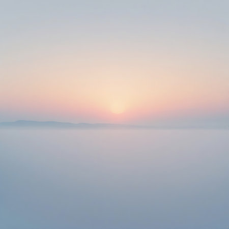 A serene and atmospheric view of a sunrise or sunset over a misty or hazy horizon. Distant, soft mountain silhouettes are barely visible. The sky is filled with subtle pastel hues, transitioning from soft pinks and yellows near the sun to pale blues and purples, creating a peaceful and ethereal ambiance.の素材