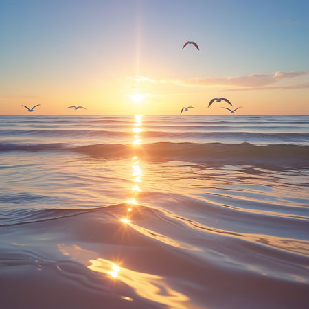Several seagulls are captured in flight above the calm surface of the ocean during sunrise. The sun, low on the horizon, creates a brilliant sunburst and casts a golden reflection on the gentle, rippling waves. Soft clouds dot the pale blue sky, contributing to a serene and beautiful seascape.の素材