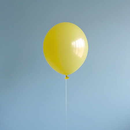 A single, bright yellow balloon is captured floating against a plain, light blue background. A thin white string hangs from the balloon, suggesting it is tethered. The image is clean and minimalist, focusing on the simple form and color of the balloon.の素材