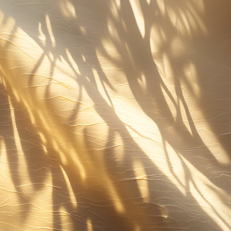 A textured surface, possibly fabric or paper, is illuminated by warm golden light. Organic, tree-like shadow patterns are cast across it, creating a dappled and atmospheric effect. The subtle lines and curves of the texture are emphasized by the interplay of light and shadow.の素材