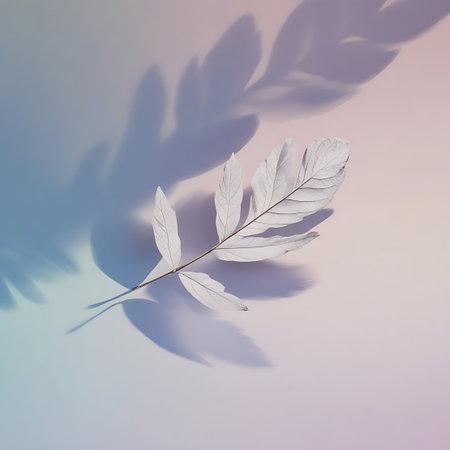 A single white leaf branch is presented against a soft pastel gradient background that shifts from pink to blue. The leaves on the branch are detailed, and the entire composition is softened by abstract, elongated shadows of foliage cast across the background, suggesting natural light filtering through.の素材
