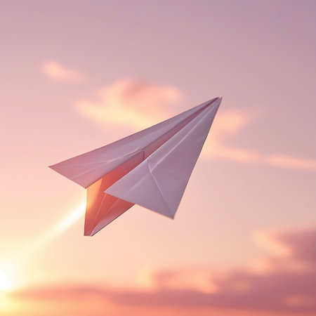 A white paper airplane is captured mid-flight against a soft, ethereal sunset sky. The sky is a gradient of pale pink and orange hues, with blurred, wispy clouds. A bright, warm light emanates from the left side, casting a glow on the airplane's folded wings. The image evokes a sense of freedom, imagination, and gentle aspiration.の素材