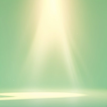 A soft, diffused yellow light beam emanates from the top of the image, casting a gentle glow on a pale green background. The light creates subtle gradients and highlights on the surface below, suggesting an empty studio or stage. The overall mood is serene and atmospheric.の素材