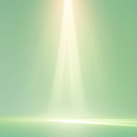 A bright, concentrated beam of light shines down from the top center of the image, illuminating a smooth, pale green surface that appears to be a floor or stage. The light spreads out as it descends, creating a soft glow and subtle shadows. The background is a uniform, soft green.の素材