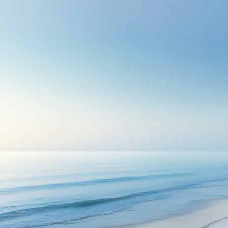 A minimalist seascape featuring a soft blue sky transitioning to a pale horizon line. Gentle, light blue waves roll onto a pale sandy beach in the foreground. The overall impression is one of extreme calm and serenity with a clean, uncluttered aesthetic.の素材