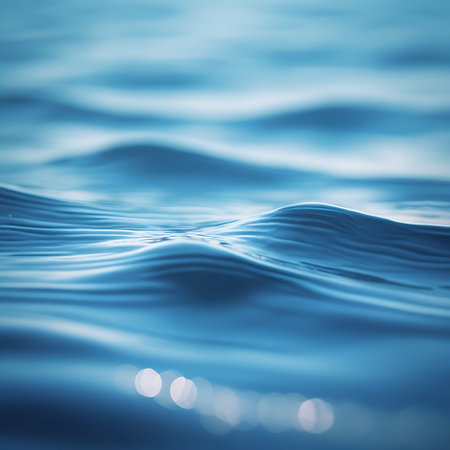 An abstract representation of blue water's surface, characterized by smooth, flowing waves and subtle ripples. Soft, out-of-focus light reflections are present, adding a gentle shimmer to the liquid. The image evokes a sense of calmness, purity, and the natural beauty of water in motion.の素材