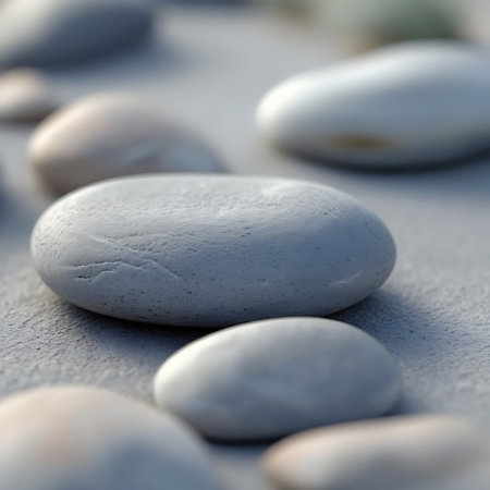 A detailed close-up shot of several smooth, rounded pebbles in shades of white and grey resting on a textured, light grey surface. The shallow depth of field blurs the background, emphasizing the tactile quality and subtle variations in color and texture of the pebbles in the foreground.の素材