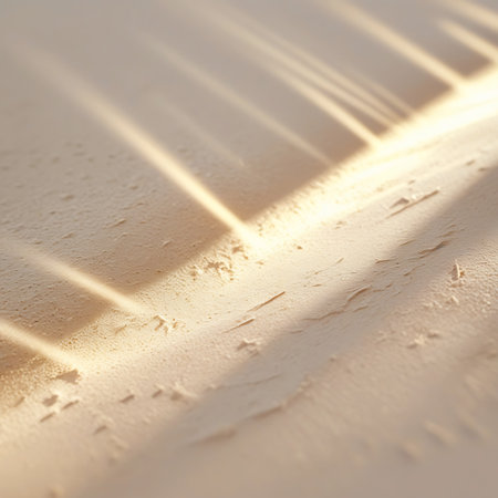 Diagonal streaks of warm, golden light cast subtle shadows across a textured, sandy surface. The diffused light creates a soft, abstract pattern, highlighting the fine grain and unevenness of the surface. This image evokes a natural, tranquil outdoor setting.の素材