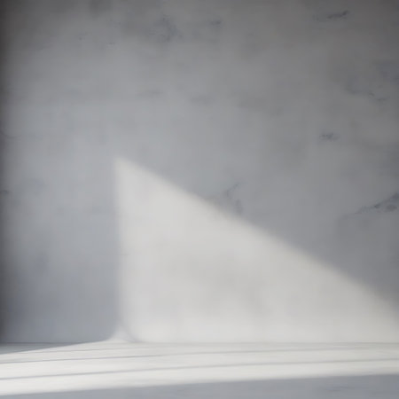 A minimalist interior scene featuring a textured concrete wall with a subtle marbling effect. A sharp, diagonal beam of sunlight casts a distinct shadow across the wall and onto the floor. The floor is also a light gray, creating a clean and simple aesthetic. The lighting is dramatic and highlights the textures.の素材