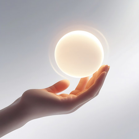 A human hand is gently supporting a luminous orb of light. The sphere emits a soft, warm glow, creating an atmosphere of tenderness and care. The clean, white background highlights the interaction and the radiant quality of the light.の素材