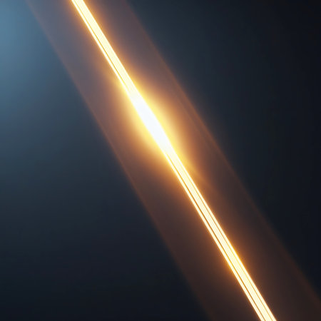 A diagonal streak of bright yellow and orange light cuts across a dark, subtly blue-toned background. The streak exhibits a strong lens flare effect, with radiating lines and a luminous core, suggesting intense energy or motion. The composition is abstract and minimalist.の素材