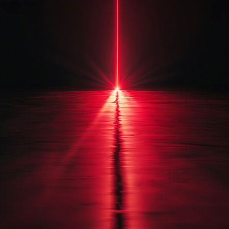 A single, intense red laser beam pierces the darkness, striking a dark, reflective surface. The beam creates a bright, glowing reflection that stretches across the surface, illuminating the surrounding area with a vibrant red hue. The overall effect is abstract and dramatic, suggesting energy and technology.の素材