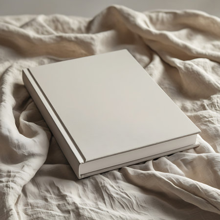 A blank beige book is angled on a surface of softly crumpled light-colored fabric. Clear details and vibrant colors enhance visual appeal.の素材