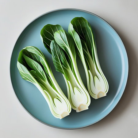 Three bok choy stalks with lush green leaves and pale white stems are positioned on a blue plate. Clear details and vibrant colors enhance visual appeal.の素材