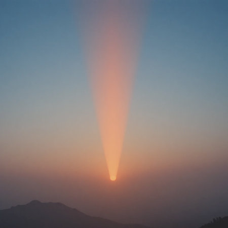 A single, bright sunbeam descends from the hazy sky, illuminating the horizon above silhouetted mountains.の素材