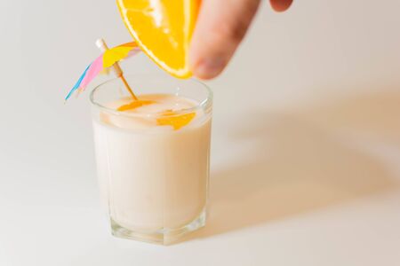 Squeeze juice from an orange into a glass of yogurt with a multi-colored umbrella and slices of orange next to the chopped orangeの写真素材