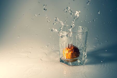 Orange mandarin drops in a glass with water on a cold background drops and splashes of water