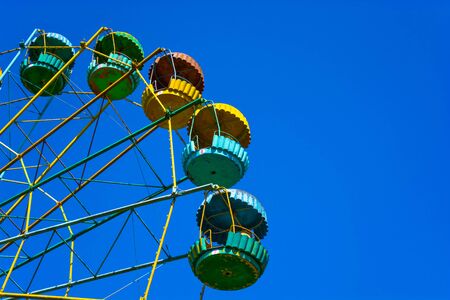 Old ferris wheel in a city park. Multi-colored booths on a background of clear blue sky.の写真素材
