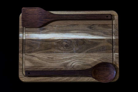Hardwood oak kitchen board on black background with wooden spoon and kitchen spatula.の写真素材