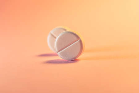 Two pills in an orange-pink background. Medical theme. Selective focus.の写真素材