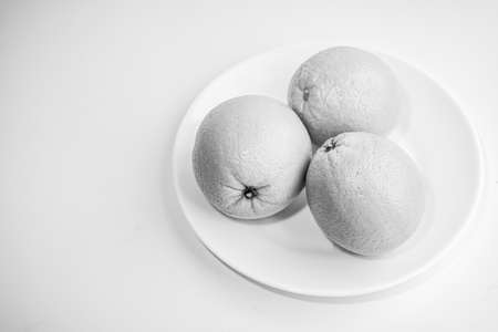 Three oranges in a plate on a white background. Black and white photo. Still life. Selective focus.の写真素材