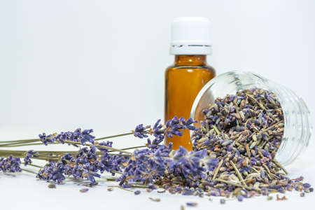 Glass bottle for aromatherapy oil with dried lavender flowers and dried seeds on a white table. Body care and aromatherapy spa massage concept.の写真素材