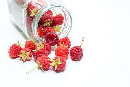 Scattered red raspberries from a glass jar on a white background. Juicy red berries. View from above.の写真素材