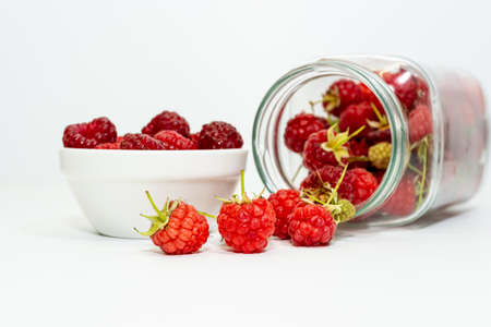Freshly picked red raspberries in a small bowl and in an inverted glass jar on a white background.の写真素材