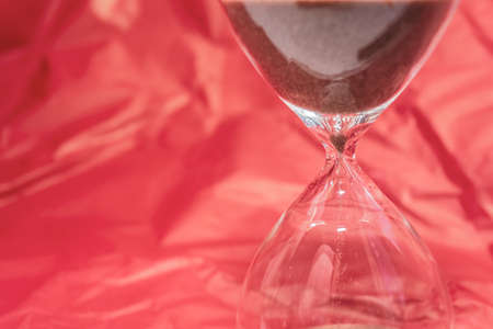 Hourglass on a red wavy silk background. Luxury and time concept concept. Nothing is eternal. The sand passes through the glass bulbs of the watch. Place for your text.の写真素材