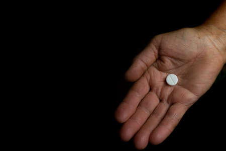 White pill on the open wrinkled palm of an old woman. Request for help. Grandmothers hand on a black...