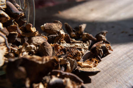 Dried mushrooms scattered from a glass jar on a wooden table illuminated by the sun. selective focus. Culinary theme.の写真素材