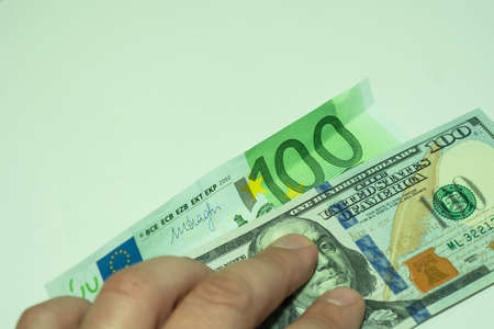 Two banknotes are pressed by the fingers of the hand. 100 dollars and one hundred euros on a light...