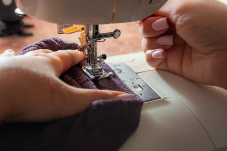 Sewing machine with fabric on thread, presser foot close-up. Female hands. The process of sewing clothes at home.の写真素材