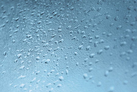 Close-up of a surface covered with water droplets. The droplets vary in size and create a textured, cool-toned pattern that conveys a sense of freshness and moisture.の写真素材