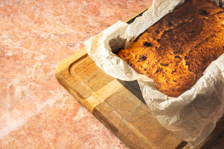 A freshly baked cheesecake with a rich golden brown crust lies in a black pan lined with parchment...