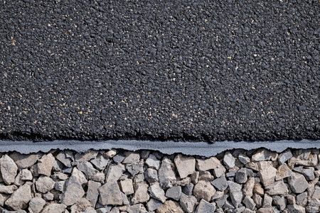 A detailed look at newly poured asphalt blending seamlessly with rough gravel beneath. This image captures the contrast between smooth black pavement and earthy tones of stones.の素材