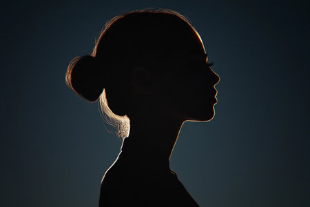 A graceful silhouette of a woman stands elegantly in profile against a dark backdrop. The soft light outlines her features, creating an air of mystery and serenity in the twilight hours.の素材