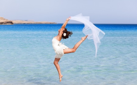 Woman in white dress is jumping near the seaの写真素材