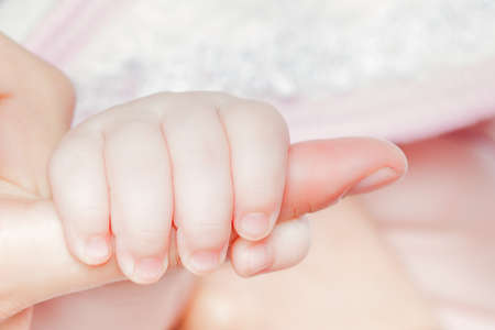 Small baby's hand is holding mother's finger