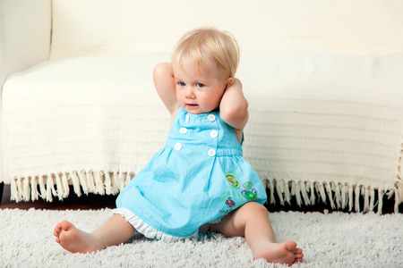 Little child is sitting on the floor near the sofaの写真素材