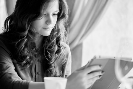 Black and white photo of young smiling woman drinking coffee in a cafe and holding a tablet computer in handsの写真素材