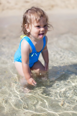 Little child girl in blue swimsuit is playing in sea waterの写真素材