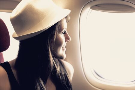 Young woman is looking through a window in the aircraft. Pastel colors