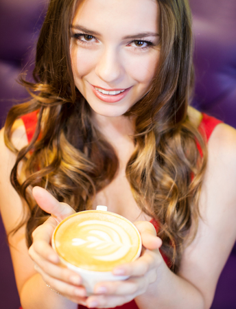a young beautiful woman in red dress is drinking coffee in a cafeの写真素材