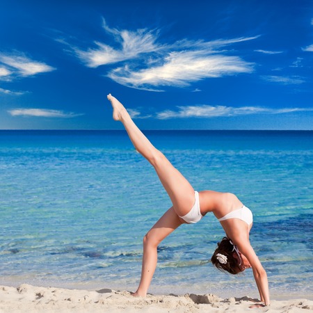 A smiling woman is doing flexibility exercise in the seaの写真素材