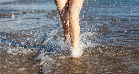 Legs of a pretty girl in red swimsuit walking in a seaの写真素材