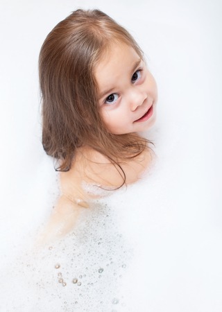 happy little girl is taking a bath with a foamの写真素材