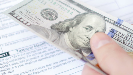 Hands counting dollars banknotes above tax form